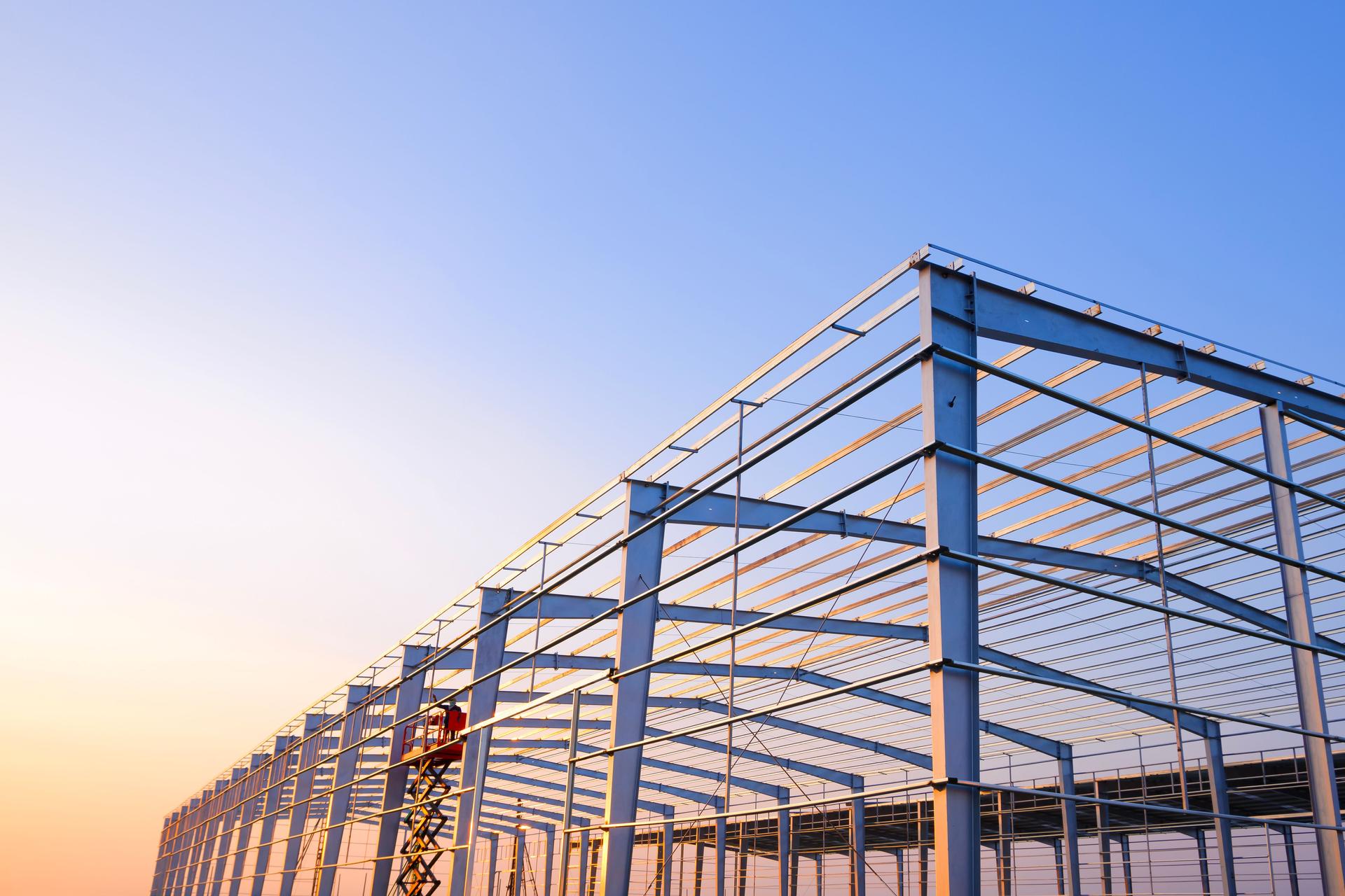 Metal posts and roof beam structure of factory industrial building framework in construction site against sunset sky background,
