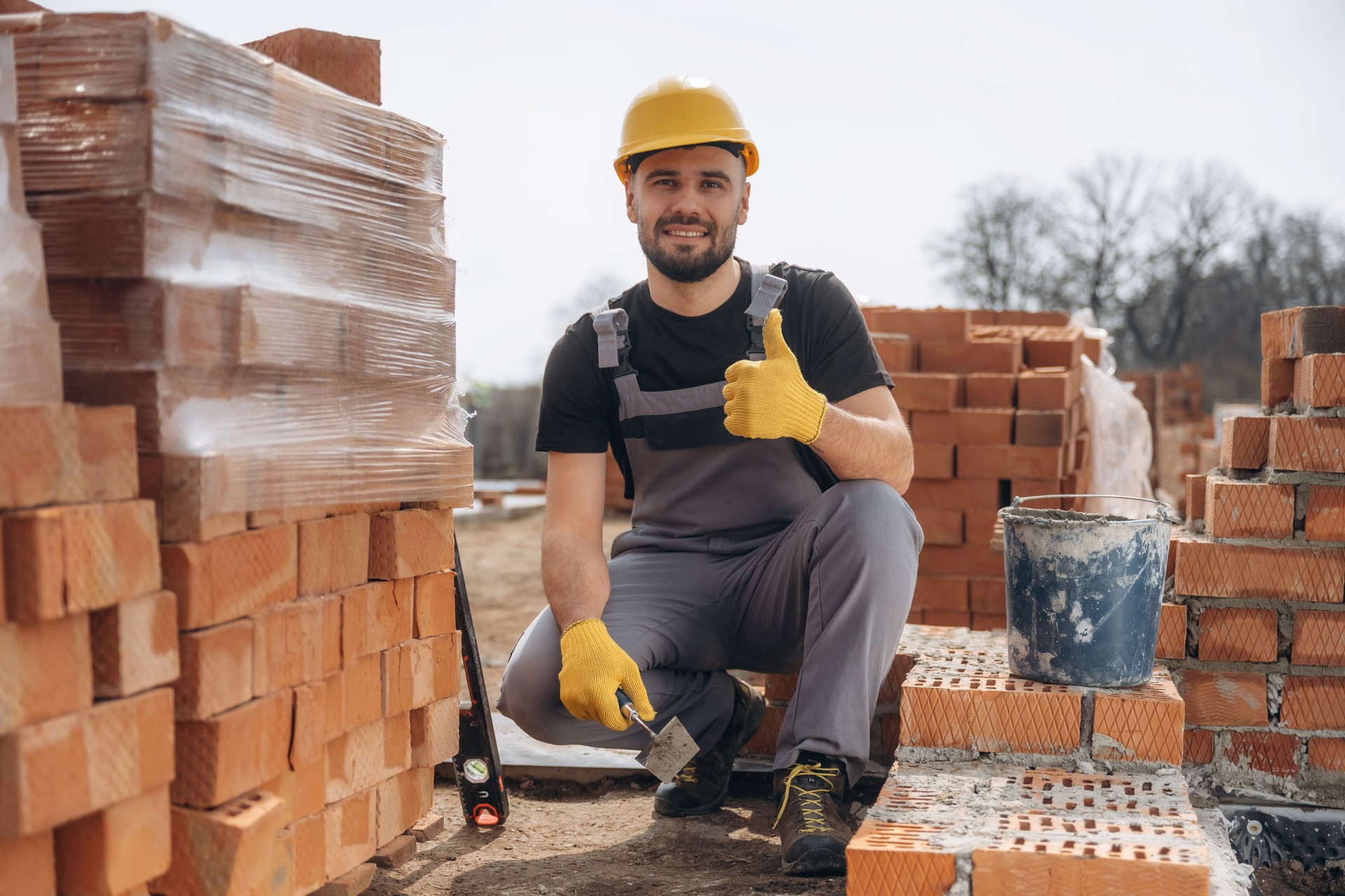 Cheerful positive guy. Construction worker is at job with bricks outdoors